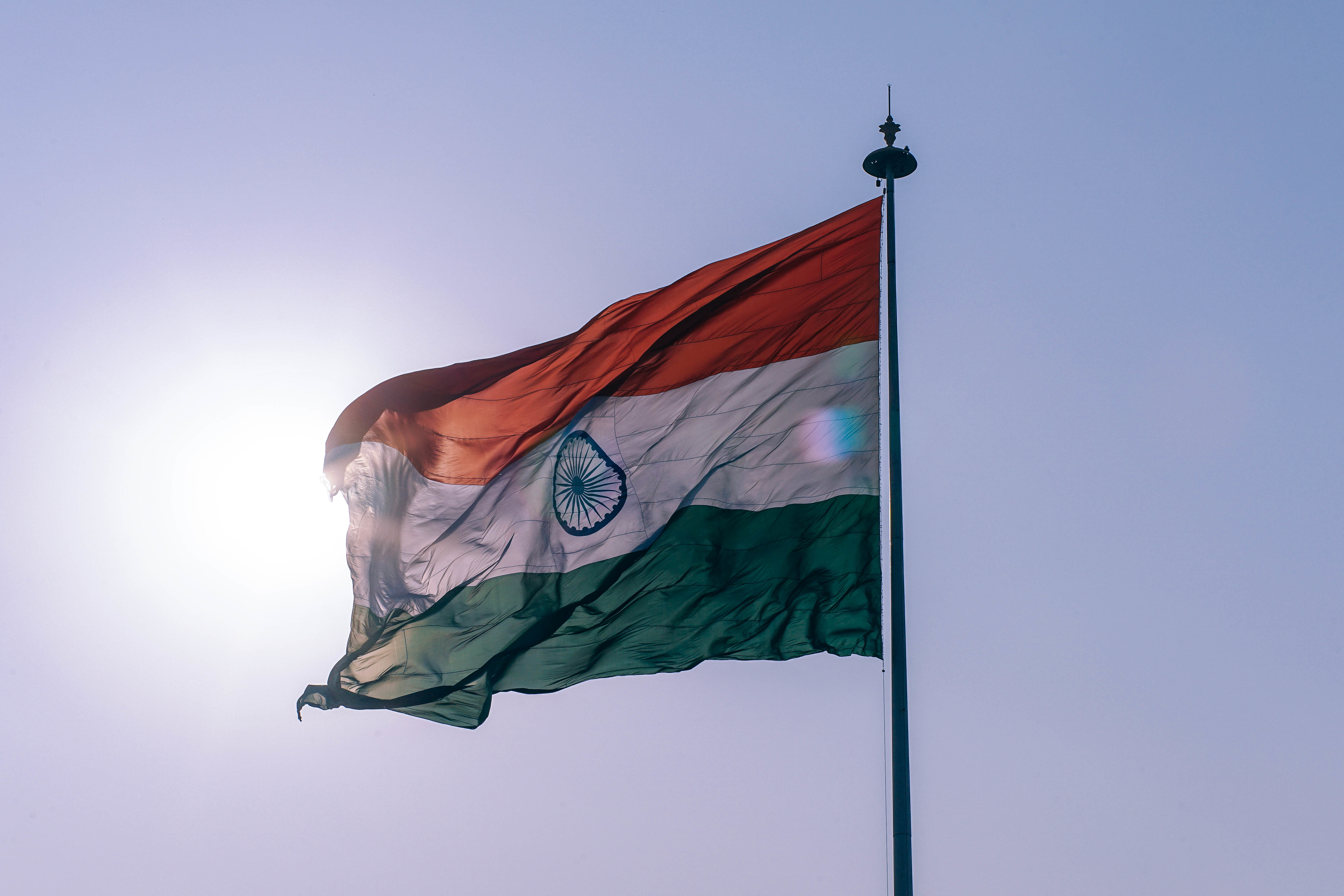 India flag flying against blue sky with sun behind